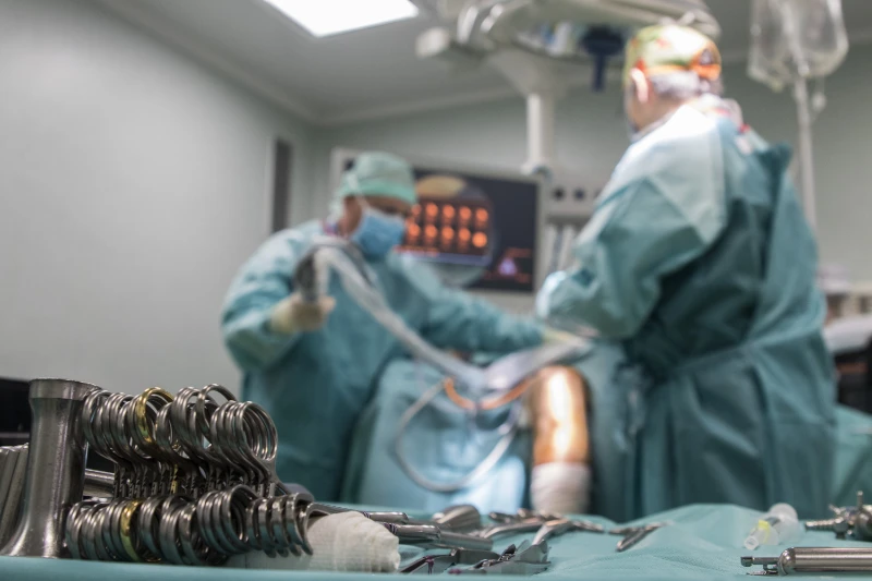 Momento de cirugía con las vistas desde la mesa de trabajo estéril, con el material y herramientas preparadas para ser utilizadas. Se ven dos doctores al fondo procediento a los preparativos iniciales de una operación de trasplante de menisco