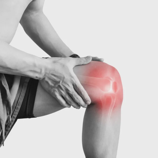 Imagen en blanco y negro de un deportista con las manos en la rodilla de la pierna izquierda que está doblada 90 grados y la zona de la rodilla pintada en rojo indicando dolor.