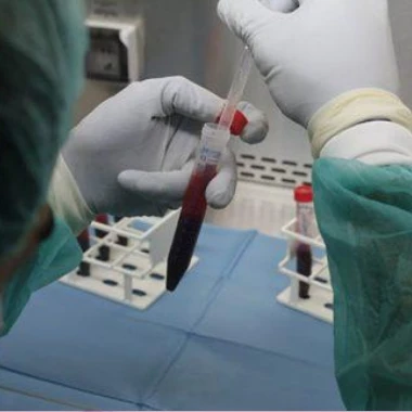 Se ven unas manos manipulando un tubo de análisis con sangre en su interior sobre una mesa con varios tubos más