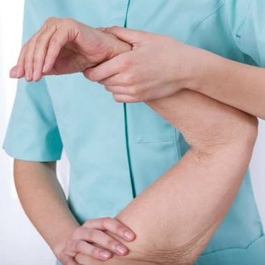 Vista del torso de un fisioterapeuta con bata verde sosteniendo un brazo de un paciente haciendo un ejercicio de recuperación de codo después de una artroscopia de codo.