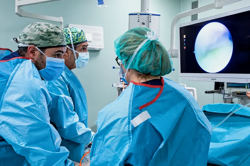 Imagen de tres médicos del Instituto Cugat que están practicando una artroscopia en un quirófano. Un doctor está comentando con una doctora que está de espaldas a la cámara, mientras otro doctor está mirando el monitor de seguimiento de la cámara de la artroscopia que queda en el lado derecho de la foto.