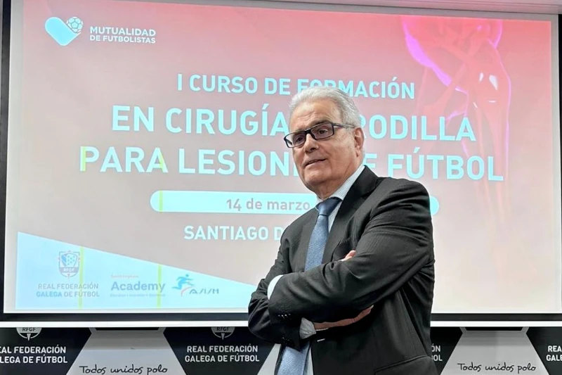 Vista del Dr. Ramón Cugat con traje y corbata en primer plano. Detrás una diapositiva del I curso de formación en cirugía de rodilla para lesiones de fútbol. Seminario que se ha realizado en Santiago de Compostela.