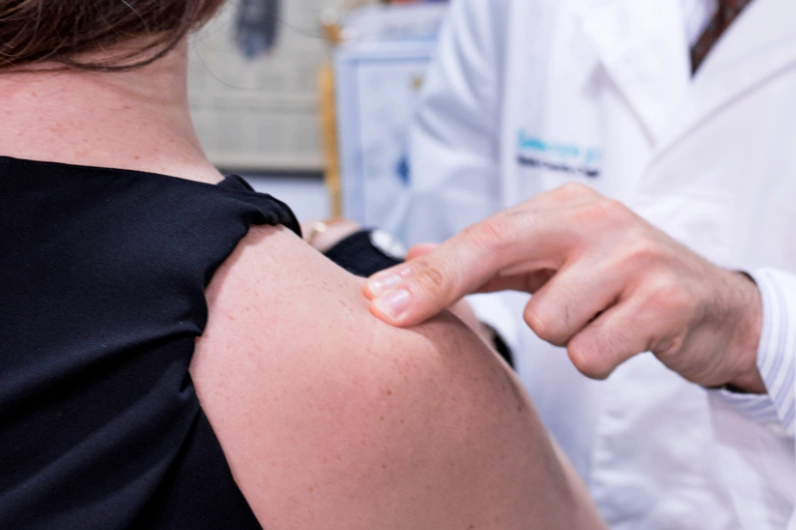 Exploración clínica del hombro por un especialista, señalando la zona subacromial del paciente durante la evaluación del síndrome de conflicto subacromial.