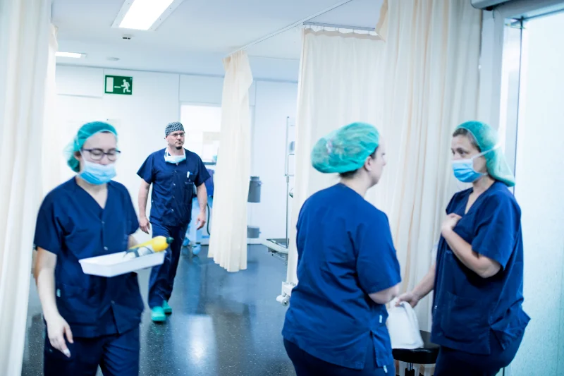 Enfermeras de quirófano del Instituto Cugat preparándose para una operación, con uniforme quirúrgico y mascarillas, en un ambiente hospitalario. Un doctor también se encuentra presente en el fondo de la foto.