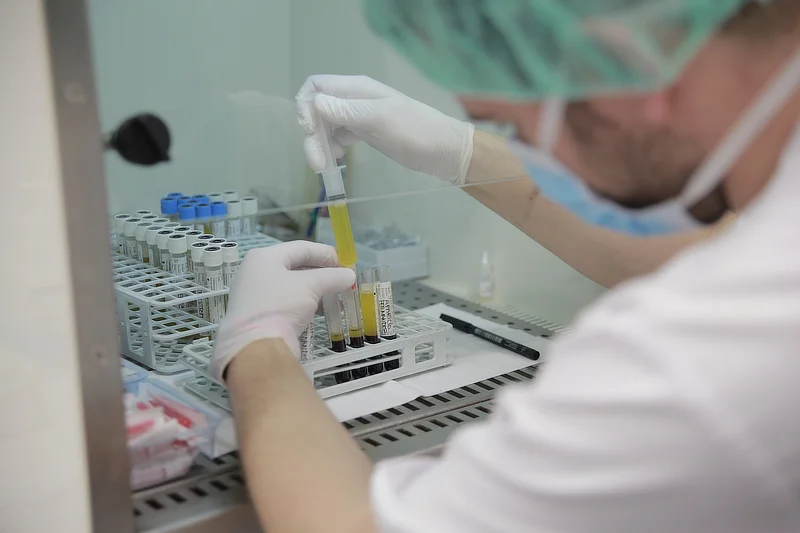 Un técnico de laboratorio con guantes y mascarilla manipulando tubos de ensayo con plasma en una cabina de seguridad. La imagen muestra el proceso de centrifugación para separar el plasma rico en plaquetas (PRP) de la sangre, esencial para terapias biológicas en el hombro. En el fondo se ven otros tubos de ensayo y equipos de laboratorio.