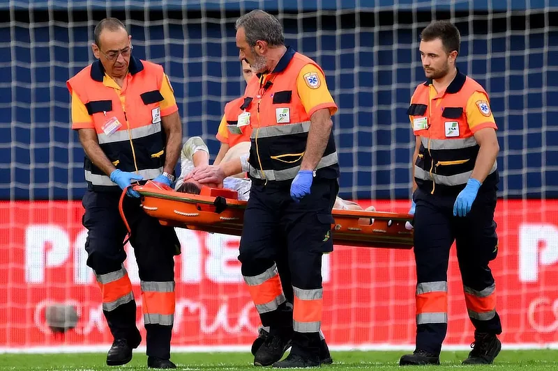 Tres paramédicos llevan a Ter Stegen en una camilla durante un partido, tras sufrir una grave lesión en la rodilla. El guardameta es retirado del campo mientras el personal médico trabaja rápidamente para trasladarlo, con la portería y la red visibles en el fondo. La imagen destaca la gravedad del incidente.