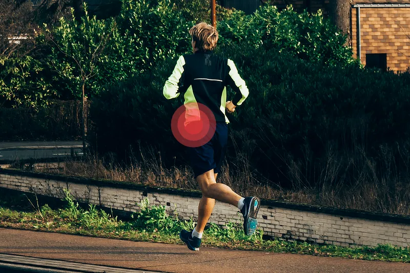 Hombre corriendo por un camino asfaltado, con ropa deportiva oscura y detalles en colores brillantes. Se observa un énfasis en su cadera derecha, representando una posible trocanteritis.