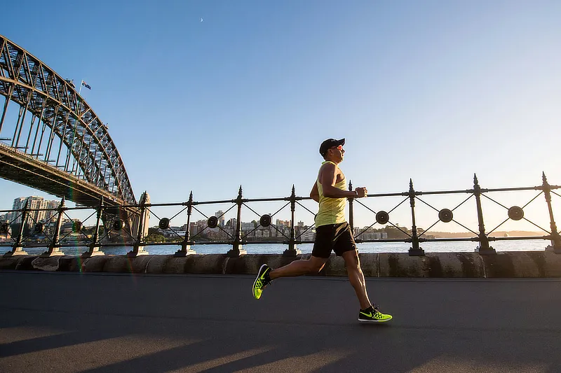 Hombre corriendo al aire libre junto a un puente al atardecer, destacando la importancia del ejercicio físico para prevenir lesiones de rodilla.