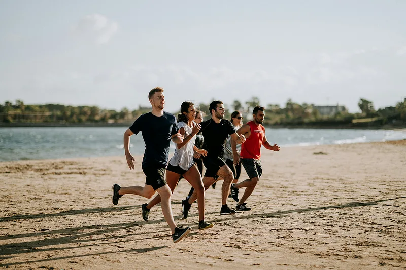 Grupo de deportistas aficionados corriendo en la playa como ejemplo de actividad física donde pueden producirse lesiones de rodilla.