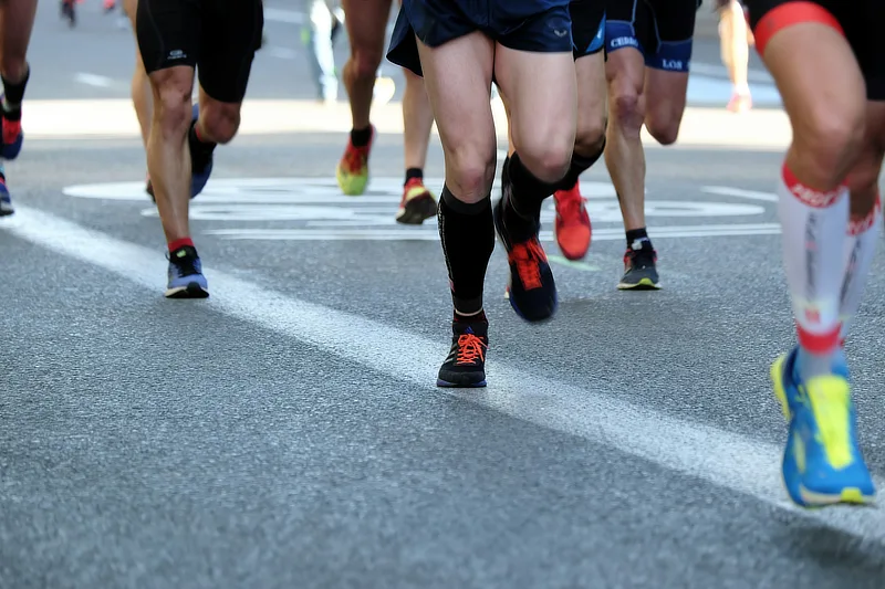 Grupo de corredores aficionados durante una competición en asfalto, con enfoque en las piernas, mostrando el impacto repetitivo que puede afectar a las rodillas.