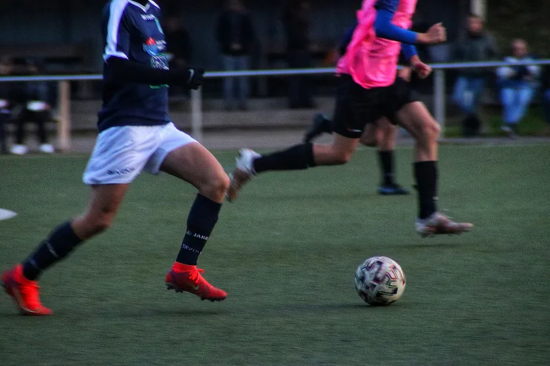Jugadores de fútbol en acción durante un partido, con un enfoque en la carrera y el contacto físico que exige estabilidad en las rodillas.
