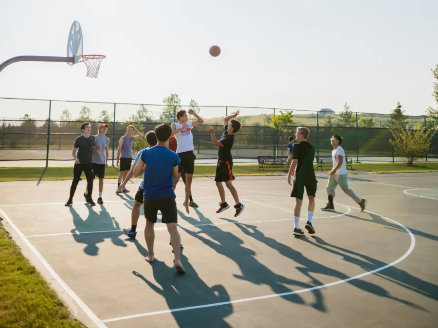 Jugadores de baloncesto en una cancha al aire libre realizando un salto y un lanzamiento, con movimientos que generan impacto en las rodillas.