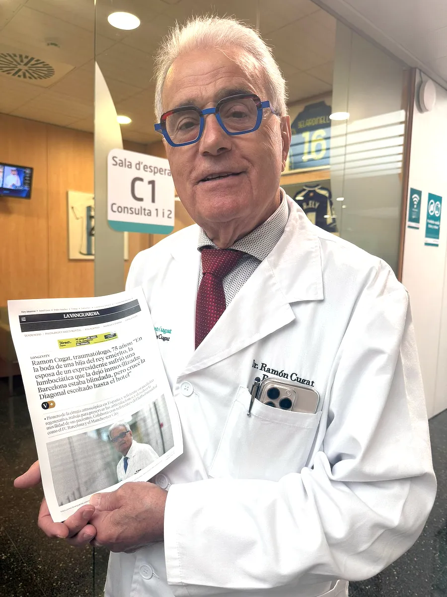 Dr. Ramón Cugat, con bata blanca y gafas azules, sostiene un ejemplar impreso de un artículo publicado en La Vanguardia sobre su trayectoria profesional.