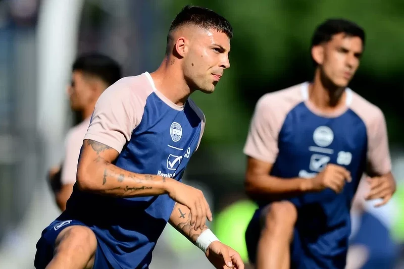 Futbolista durante un entrenamiento con camiseta azul y detalles claros, centrado en la preparación física previa al partido en campo exterior soleado.