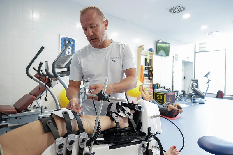 Fisioterapeuta ajustando un equipo de rehabilitación de rodilla en clínica especializada, mostrando el inicio del proceso de recuperación tras lesión.