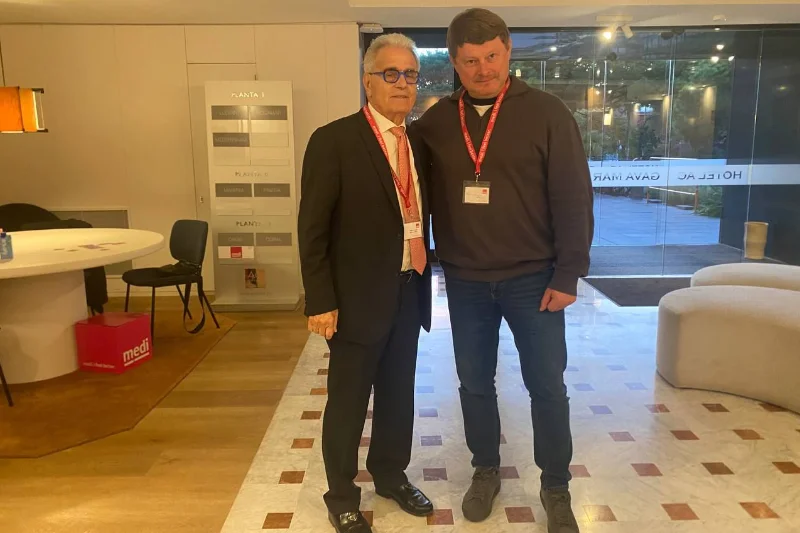 El Dr. Ramón Cugat y el Dr. Andriy Shmorgun posan juntos en el hotel sede del 6º Summit Instituto Cugat, ambos con acreditación del congreso y ambiente profesional de fondo.