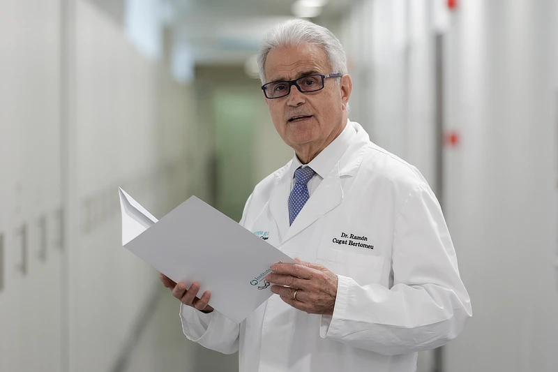 El Dr. Ramón Cugat vestido con bata médica blanca en un pasillo del Instituto Cugat mientras sostiene y lee un documento, en un entorno clínico luminoso y profesional.