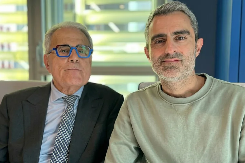 Fotografía del Dr. Ramón Cugat, con traje oscuro, corbata y gafas azules, sentado junto al periodista Carlos Mesa en un estudio para la entrevista Dr. Ramón Cugat Radio 4.