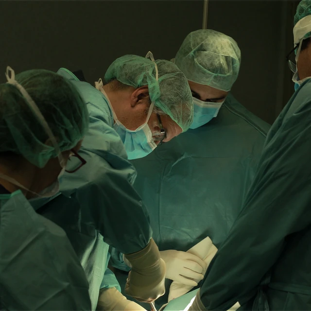 Unidad protesis – Enfoque de instituto cugat barcelona Primer plano de cuatro profesionales médicos con vestimenta quirúrgica verde, gorros y mascarillas, inclinados y colaborando estrechamente en equipo durante una intervención médica.