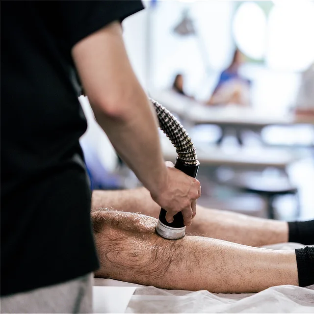 Professional applying muscle recovery technology to a patient's knee during a rehabilitation and physiotherapy session.