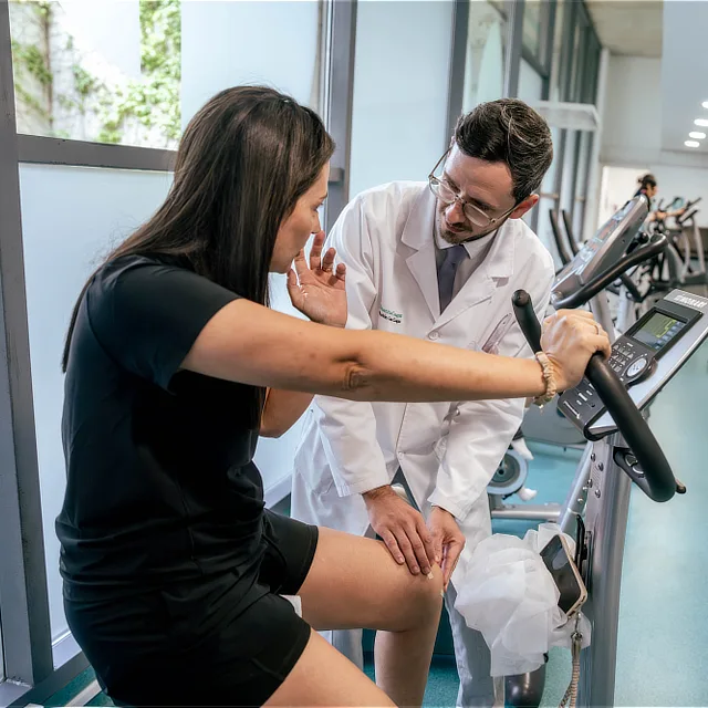A doctor at Instituto Cugat in Barcelona performing a manual knee assessment on a patient during a rehabilitation and physiotherapy session.