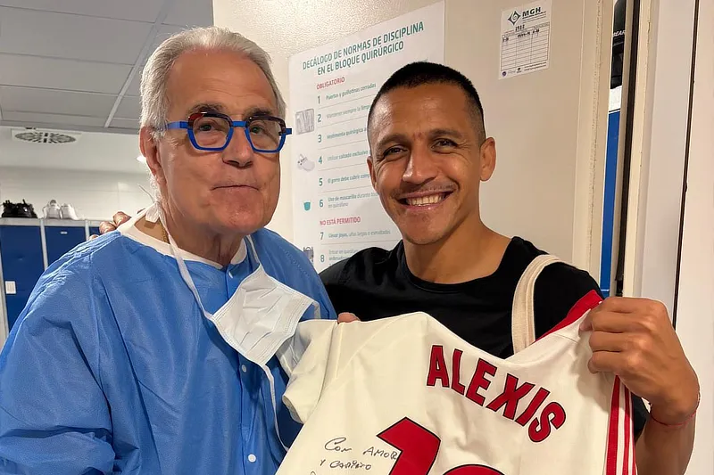 El Dr. Ramón Cugat y Alexis Sánchez posan sonrientes sosteniendo la camiseta del futbolista dedicada.