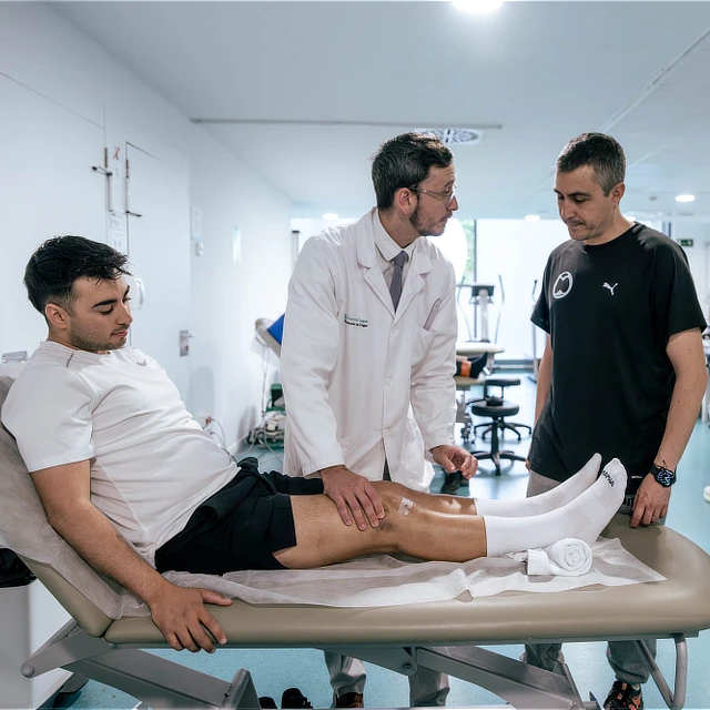 Unidad de fracturas 4 Como es el proceso de tratamiento Médico examinando la rodilla de un paciente recostado en una camilla junto a un fisioterapeuta.