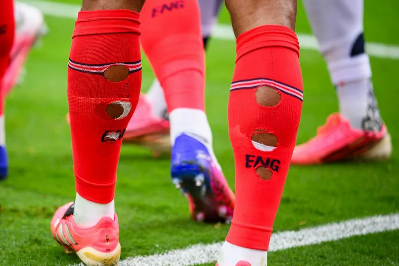Primer plano de la parte posterior de las piernas de un futbolista de la selección de Inglaterra con varios agujeros circulares recortados en sus medias rojas.