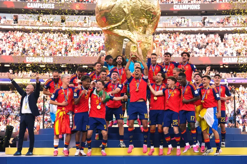 Los jugadores de la selección española de fútbol celebran con medallas y confeti dorado levantando el trofeo de campeones del mundo en el podio.