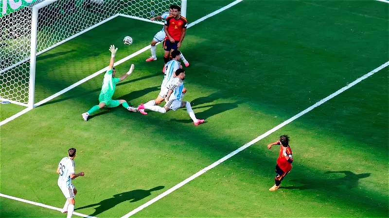 Vista aérea de una jugada de fútbol en el área donde un delantero de España remata a puerta ante la estirada del portero y los defensores de Argentina.