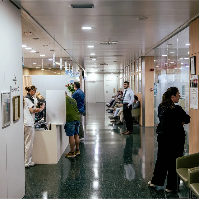 Unidad de tumores óseos 1 Cuándo debe acudir un paciente Pasillo de Instituto Cugat en Barcelona con mostrador de recepción, personal sanitario atendiendo a pacientes y varias personas esperando sentadas en la zona de consultas.