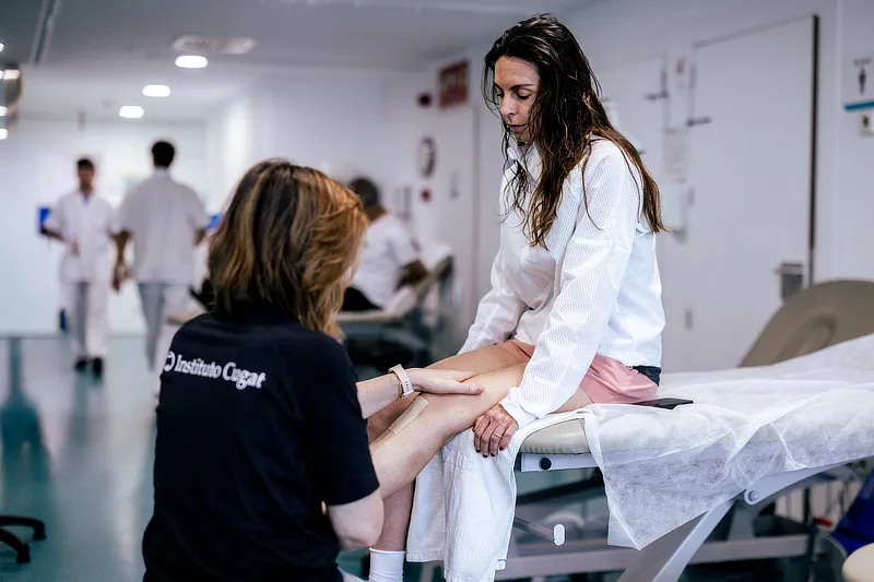 Fisioterapeuta de Instituto Cugat evaluando la movilidad de la rodilla de una paciente durante una sesión de rehabilitación.